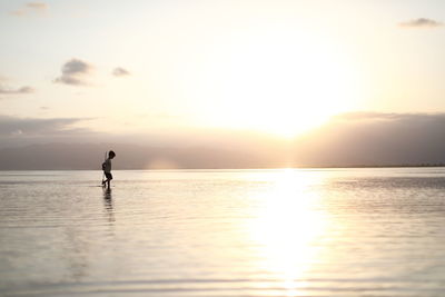 Silhouette man on sea against sky during sunset