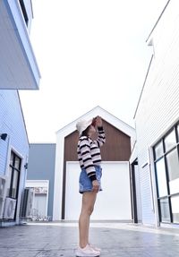 Full length of woman standing outside house against sky