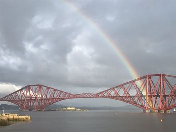 View of rainbow bridge over river against cloudy sky