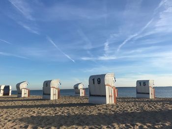 Hooded beach chairs by sea against blue sky