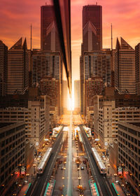Traffic on city street amidst buildings against sky during sunset