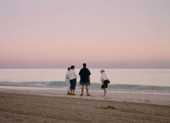 Friends walking on beach against clear sky during sunset