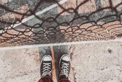 Low section of person standing by chainlink fence