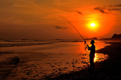 Silhouette man fishing on shore against sky during sunset