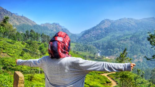 Rear view of woman with arms outstretched standing on mountain in sunny day