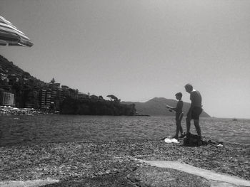 Men standing on shore against clear sky