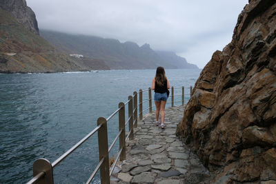 Rear view of woman standing by railing against sea