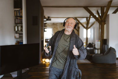 Senior man gesturing while enjoying listening to music through headphones at home