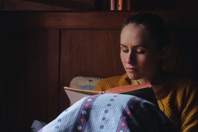 Woman reading book on bed in wooden cottage