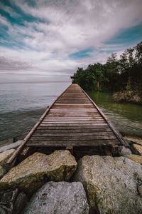 Pier on sea against cloudy sky