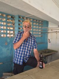 Man holding metal grate in front of face with beer bottle at abandoned building