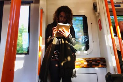 Young woman using phone while standing on bus