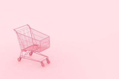 Close-up of shopping cart against pink background