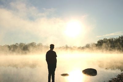 Rear view of silhouette man standing by lake against sky