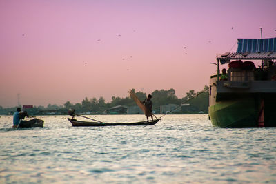 Man fishing in sea against sky during sunset