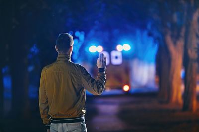 Rear view of man gesturing to ambulance while standing in forest at night