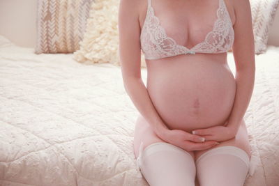 Midsection of pregnant woman in bikini sitting on bed at home
