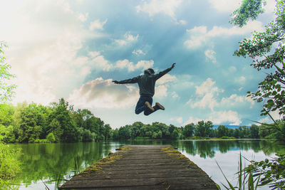 Full length of man jumping on pier over lake against sky