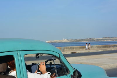 Woman holding mobile phone in old-fashioned blue car on road