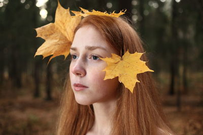 Close-up of thoughtful young woman with leaves on hair at forest during autumn