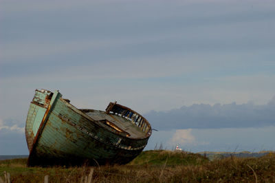 Abandoned boat on field against sky