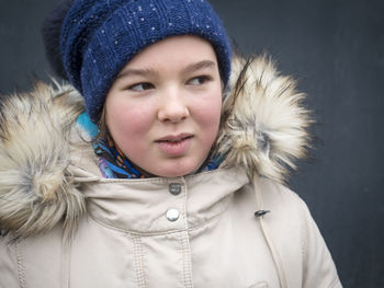 Close-up of girl wearing knit hat and fur coat during winter by wall