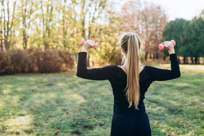 Fitness in the park, girl holding dumbbells, back view.