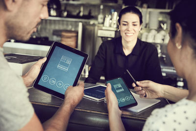 Smiling man using smart phone while women looking in cafe