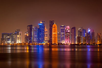 Illuminated city by buildings against sky at night