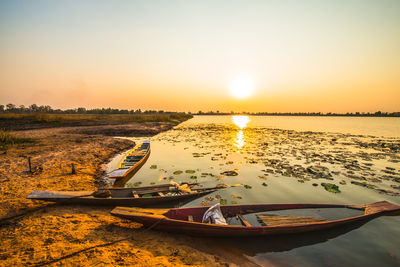 Boats moored on shore against sky during sunset