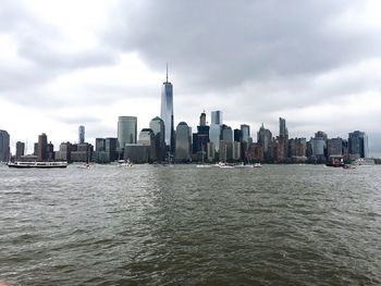 One world trade center amidst buildings by east river against sky at manhattan