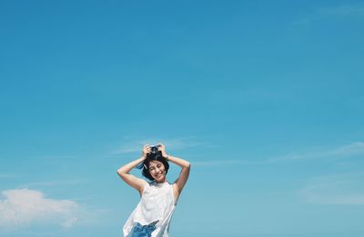 Low angle view of woman standing against blue sky