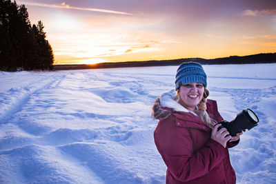 Portrait of young woman standing on snow covered landscape during sunset