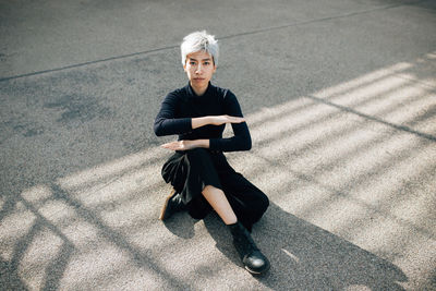 High angle view of woman gesturing equal sign while sitting on footpath 