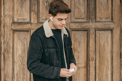 Young man using phone while standing on wood