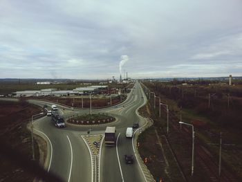 Road leading towards city against cloudy sky