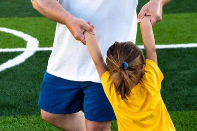 Cropped faceless father spinning daughter on sports ground