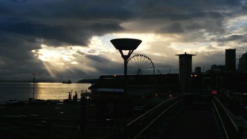 Silhouette of city against cloudy sky during sunset