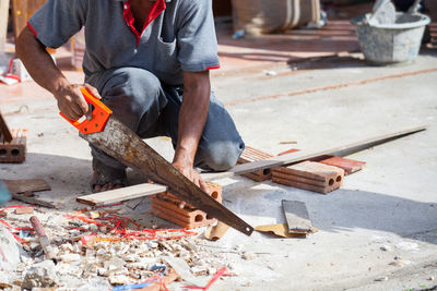 Low section of man cutting plank on floor