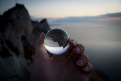 Close-up of hand holding crystal ball at beach during sunset