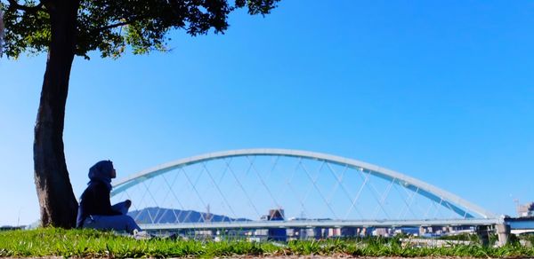 People on bridge against clear blue sky