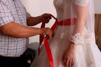 Midsection of man dressing bride at home