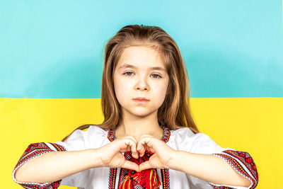 A girl in an embroidered shirt shows a heart sign as a sign of love for ukraine.