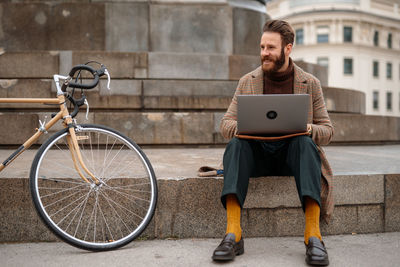 Rear view of man using digital tablet while sitting on street