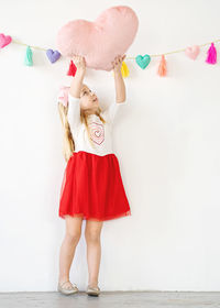 Cute young girl holding pink heart pillow up over head