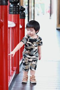 Full length of cute boy touching red railing in corridor