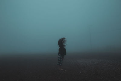 Side view of woman tossing hair while standing on field during foggy weather