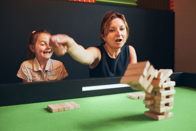 Excited woman playing jenga game with her daughter in play room. woman removing block from stack