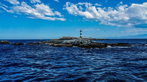 Lighthouse by sea against blue sky