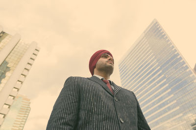 Low angle view of man looking at modern buildings against sky